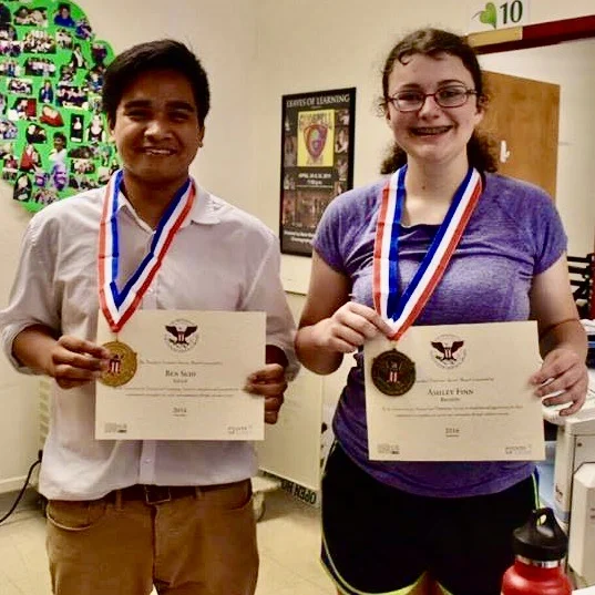 Two students wearing medals and holding certificates