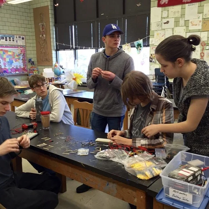 Students assembling electrical circuits with wires and components at a table