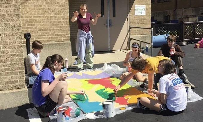Students painting a large colorful panel outdoors
