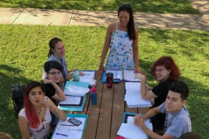 A group gathered around a picnic table with notebooks outdoors