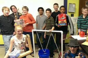 Students posing beside a frame with a bucket suspended from cords