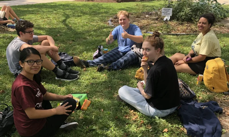 Students sitting together on the grass with snacks and backpacks