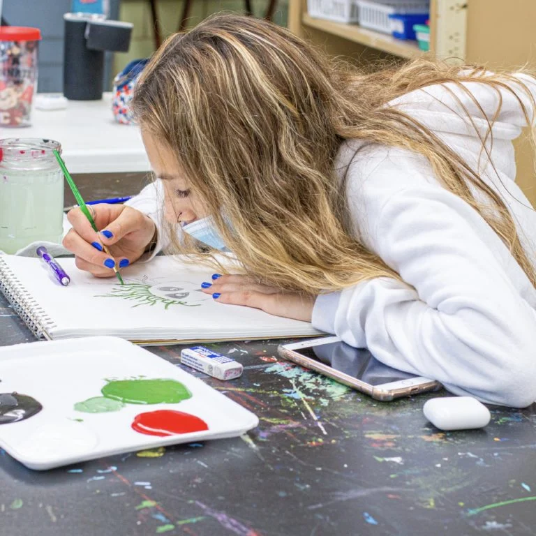 Student painting a drawing in a sketchbook