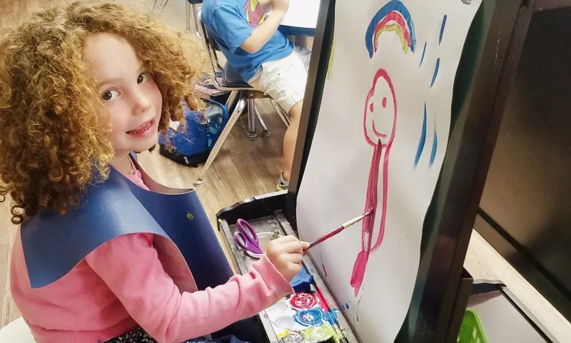 Child painting a figure and rainbow at an easel