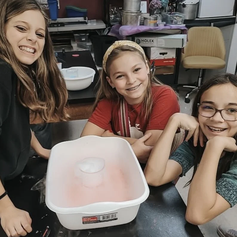 Three students gathered around a plastic tub on a classroom table