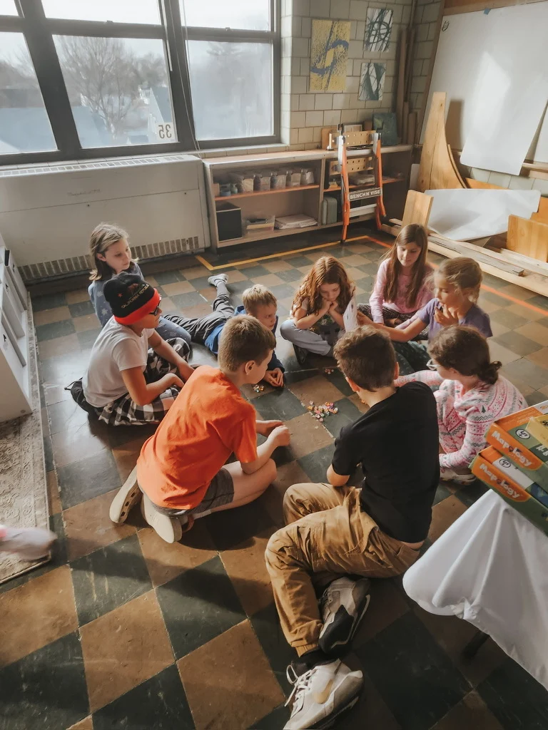 Students sitting in a circle around small objects on the classroom floor