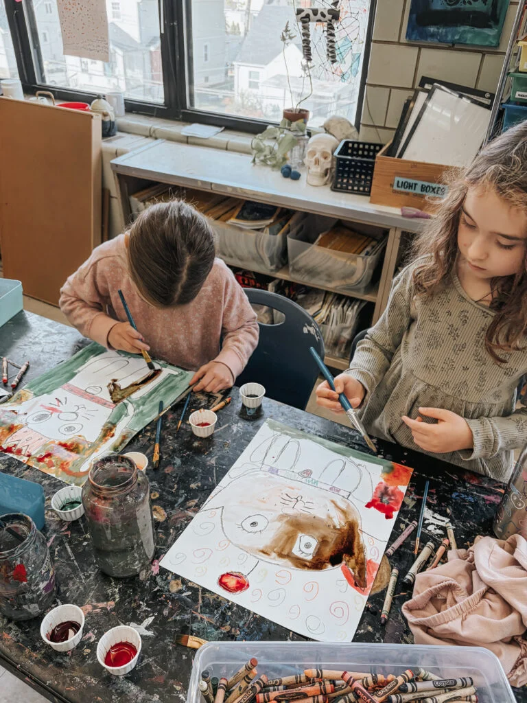 Students painting their drawings at an art table