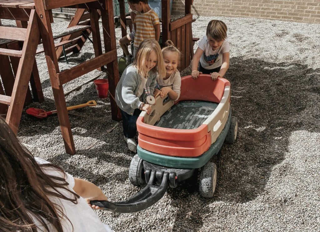 Children gathered around a water-filled wagon beside a play structure